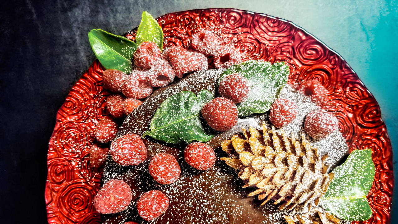 A chocolate tart decorated with raspberries, pinecones, and leaves