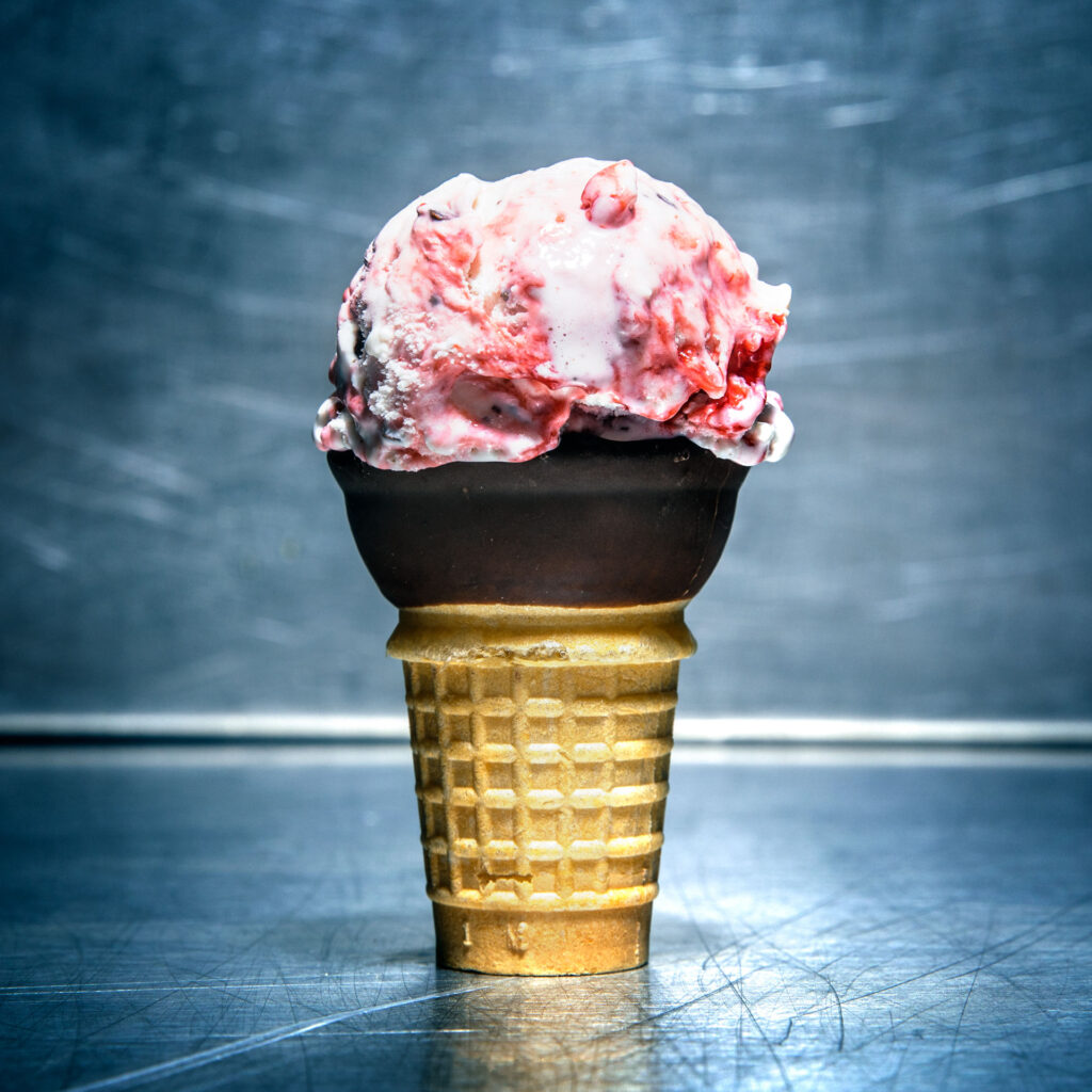 An ice cream cone containing a scoop of white chocolate ice cream with a tart cherry swirl.