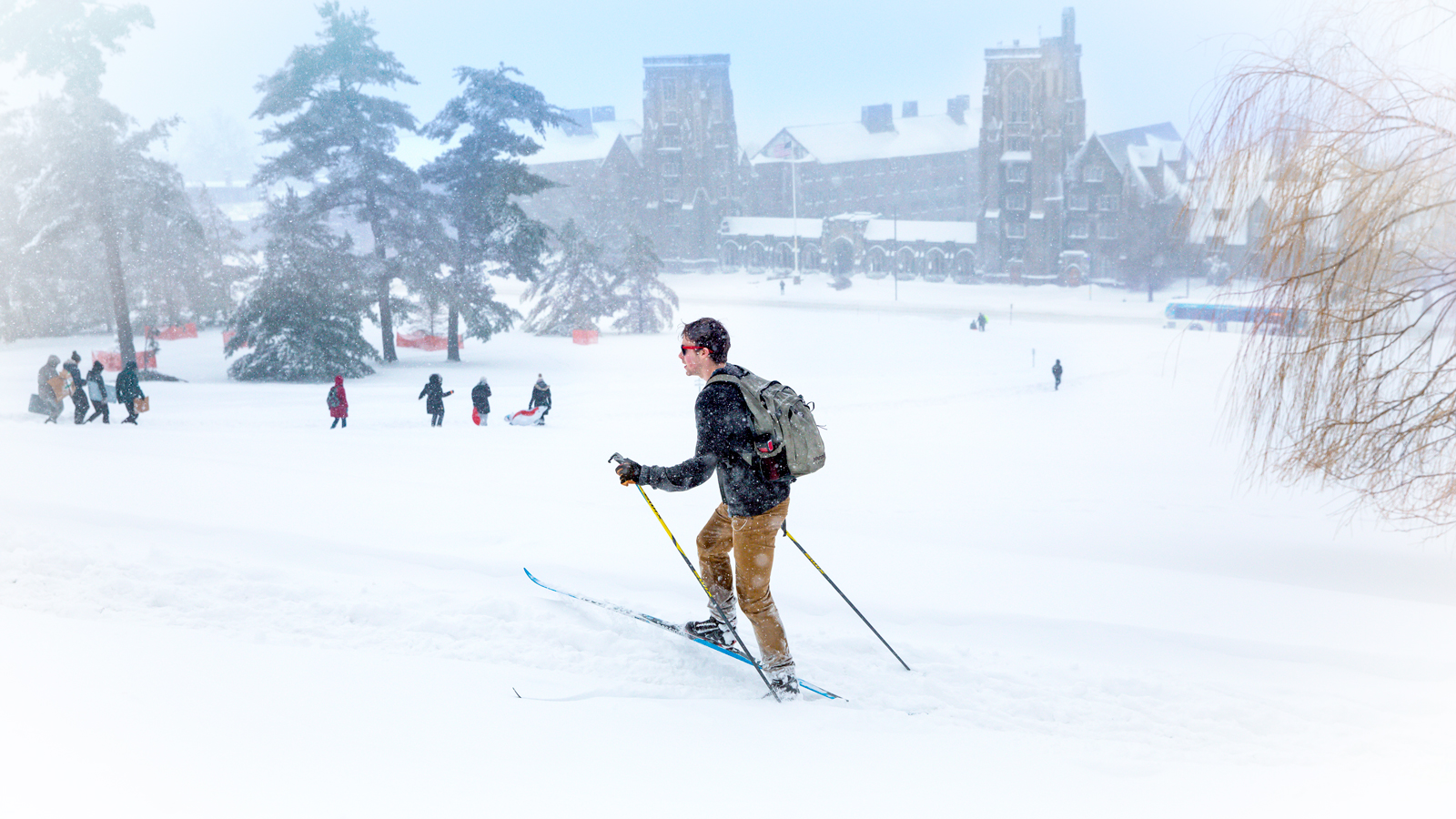 Students, including one on cross country skis, navigate their way up the hill from West Campus as fresh snow blankets campus.