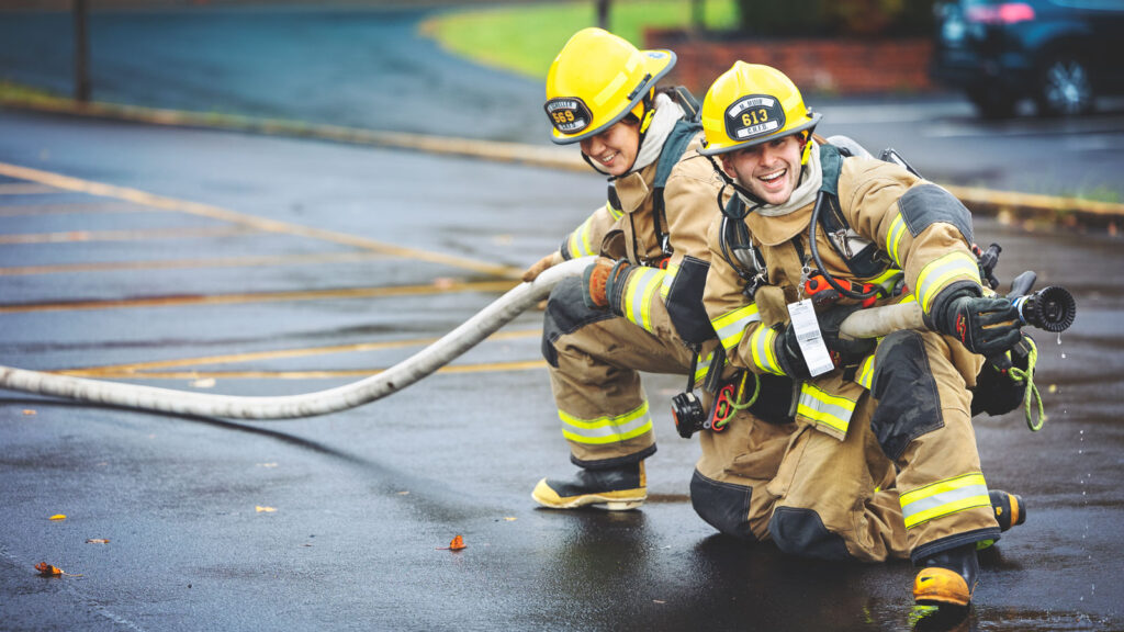 Two people in firefighter gear holding a fire hose