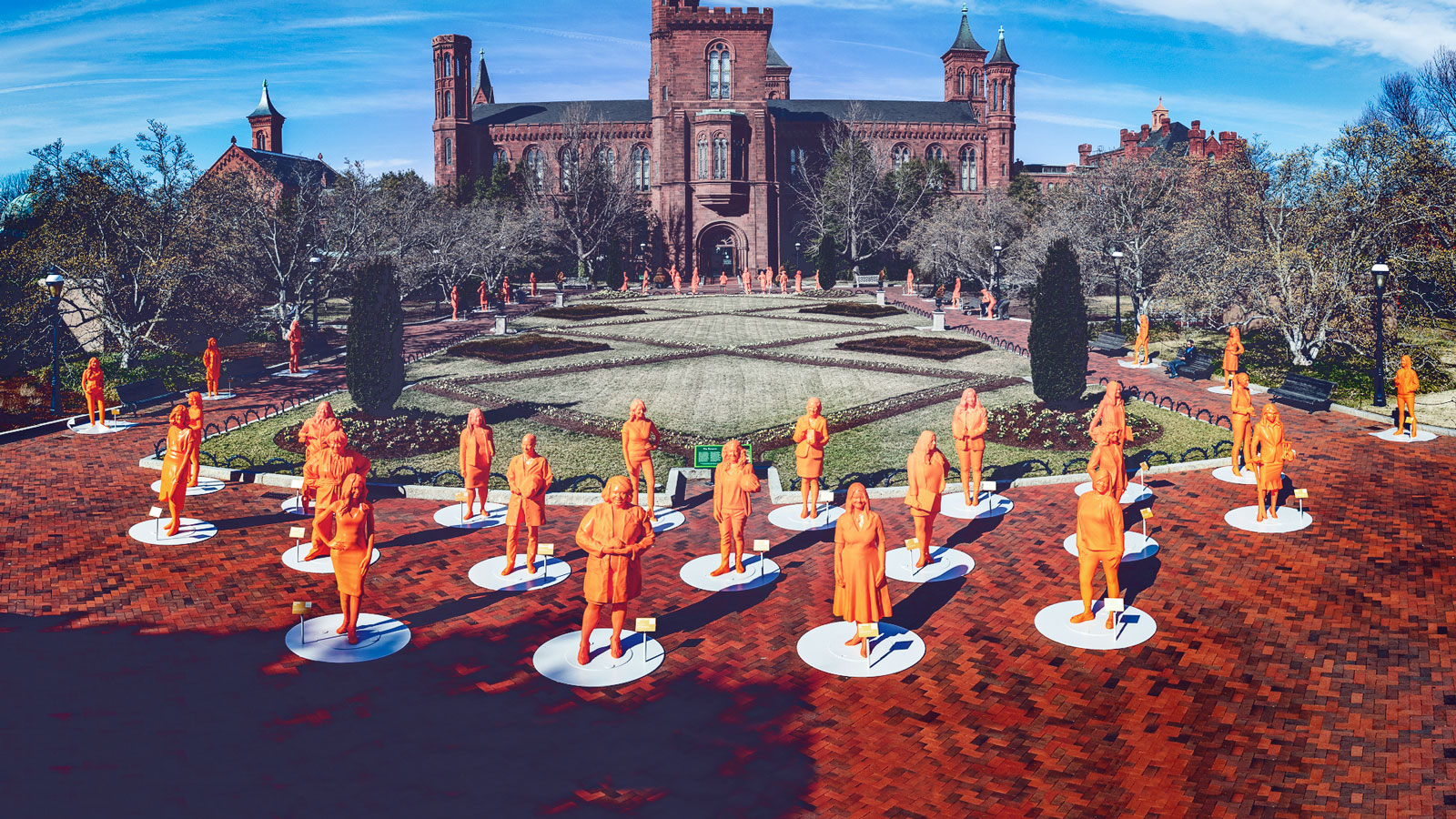 A collection of orange statues of women outside the Smithsonian 'castle'