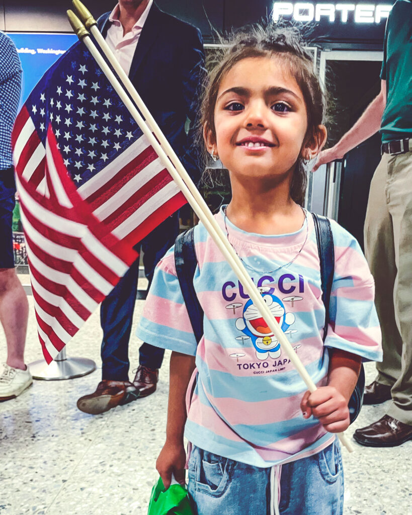 An Afghan girl in a US airport holding an American flag