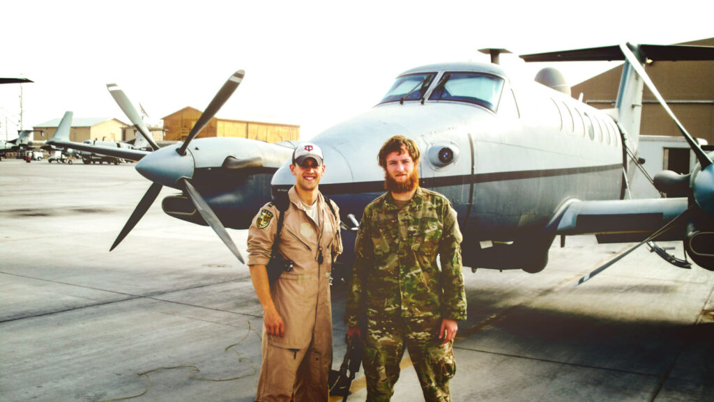 Two men in uniform in front of a plane in Afghanistan. Caruso is on the right.