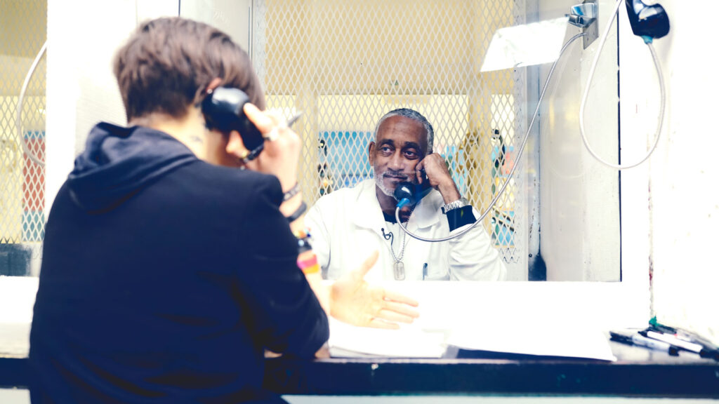 Two people talking on the phone in a prison visiting room