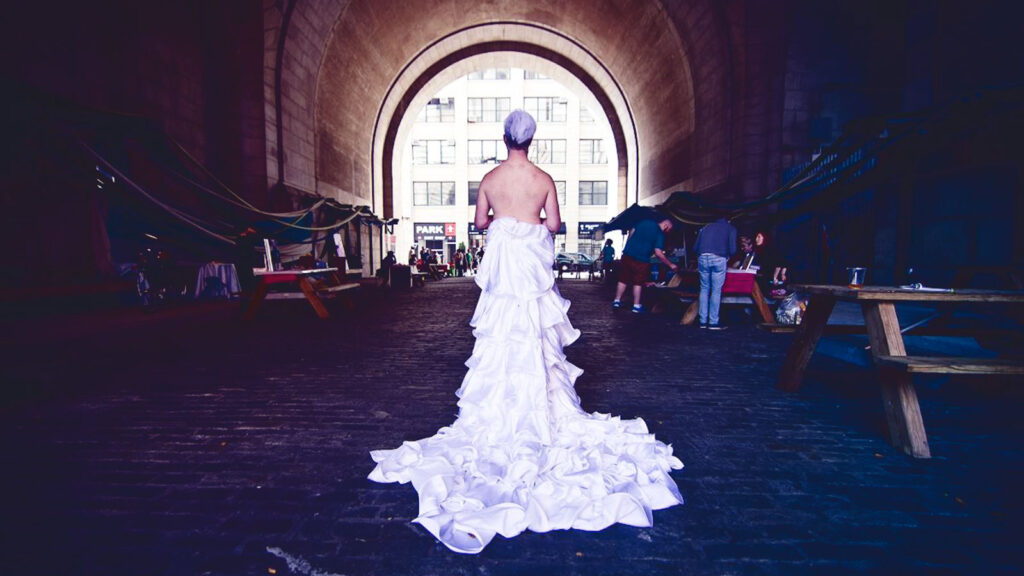 A man in a wedding gown in a tunnel, viewed from the rear