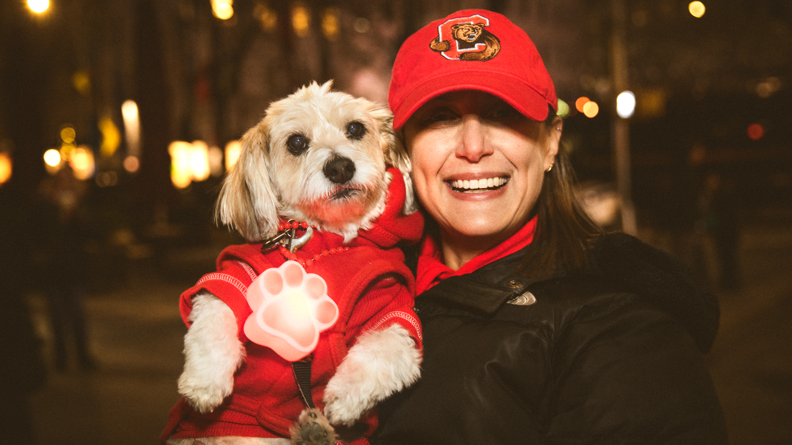 A woman with a red hat holding a small dog wearing a red sweater during the Sy Katz Parade in New York City