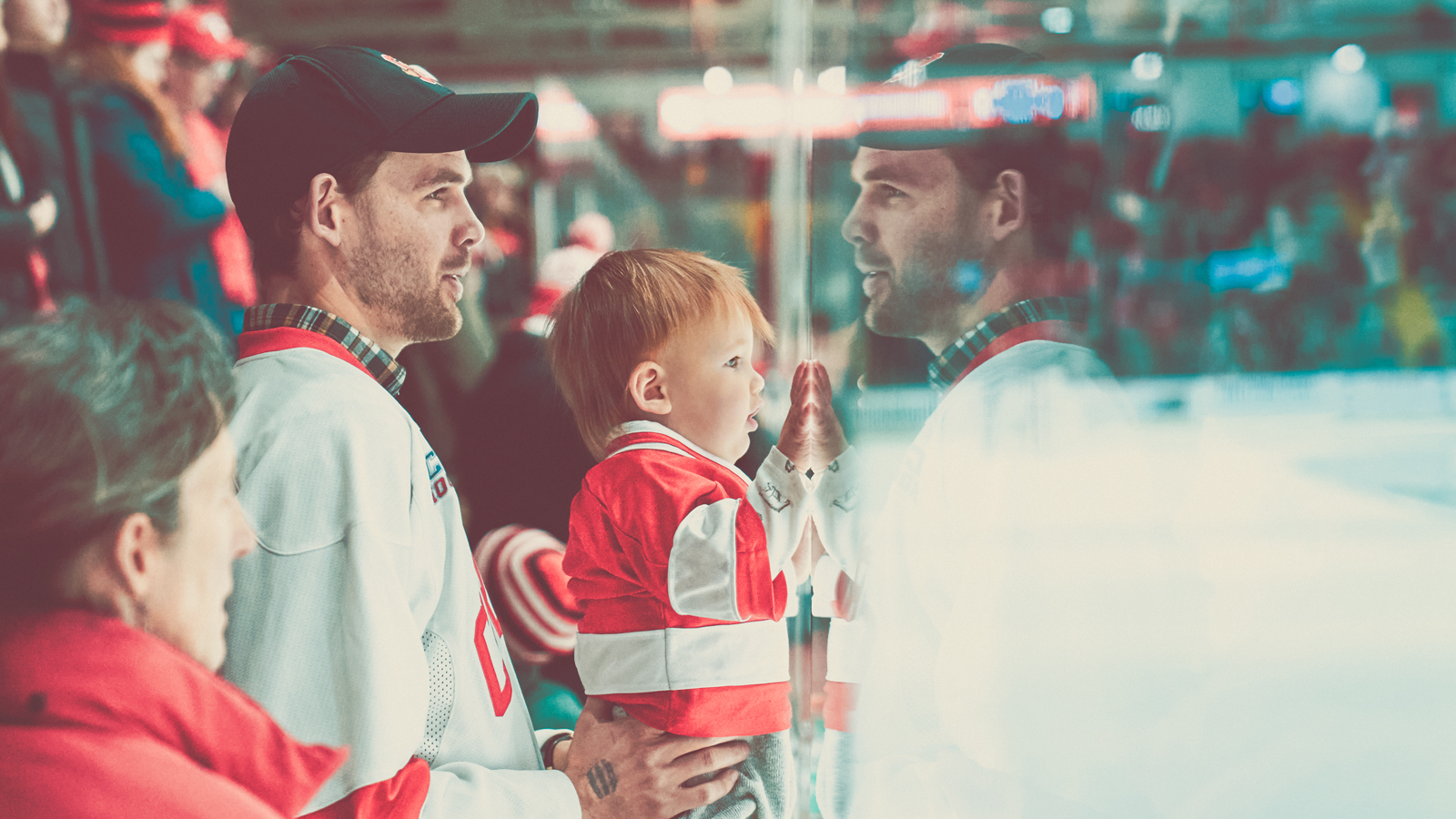 A man holding a toddler up to the glass at a Cornell hockey game.