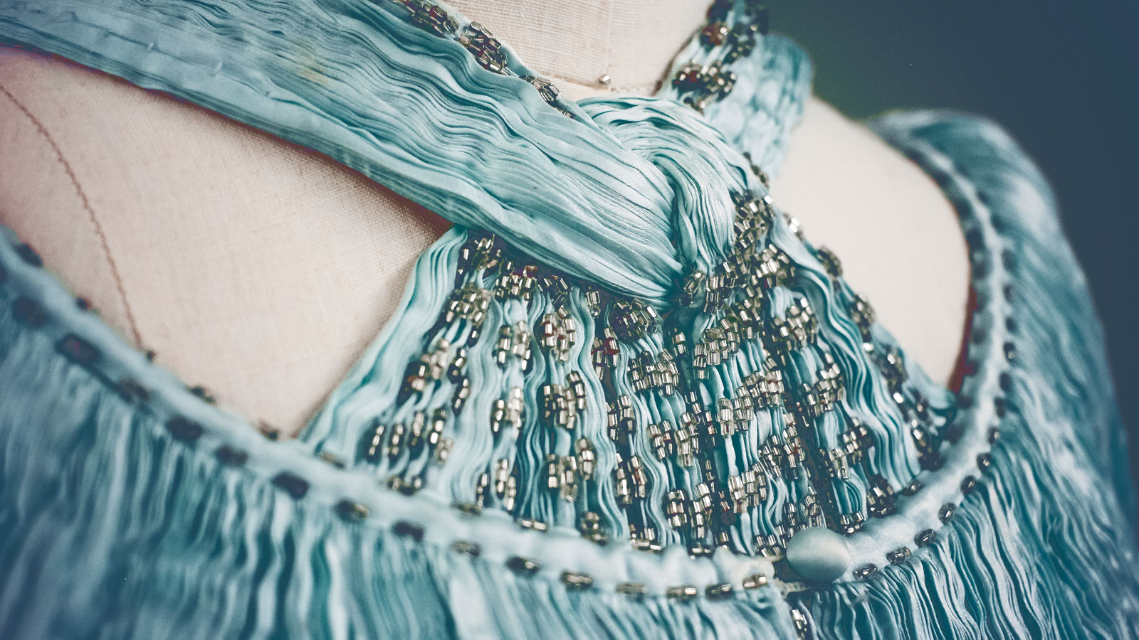 A knotted, halter-style collar of a vintage woven blue dress with silver charms in the threads.