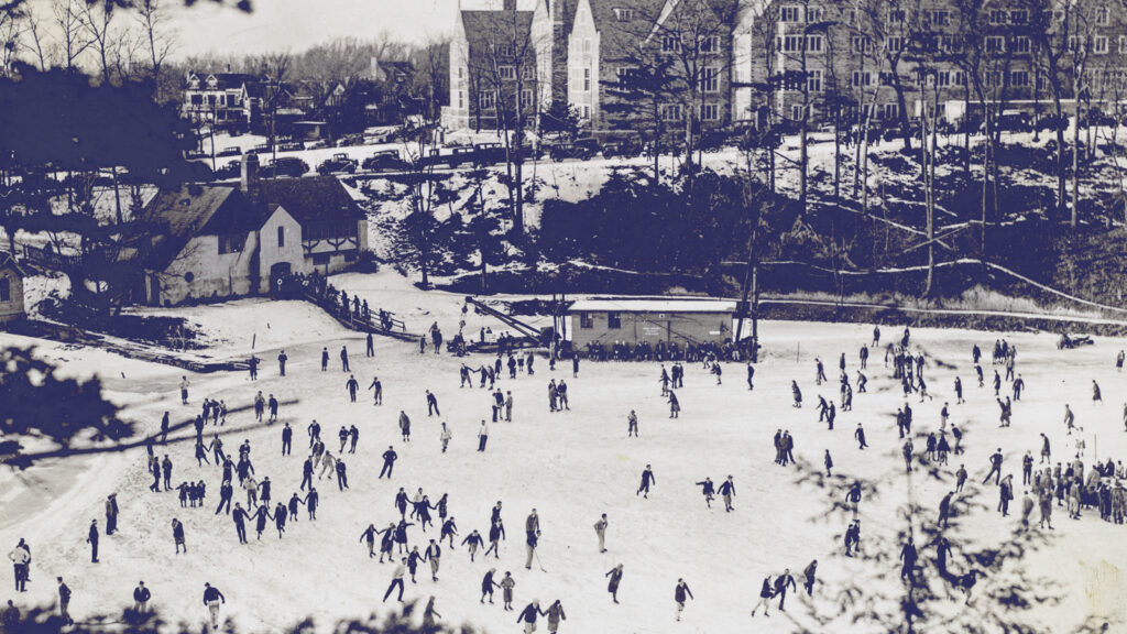 A frozen Beebe Lake on a typical winter day in the early 20th century, filled with ice skaters. The Johnny Parson Club is at left and North Campus and Balch Hall is in the background