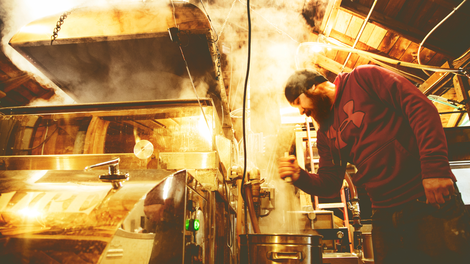 A man in a maple sugar house operating a sap boiling machine with steam coming off of it.