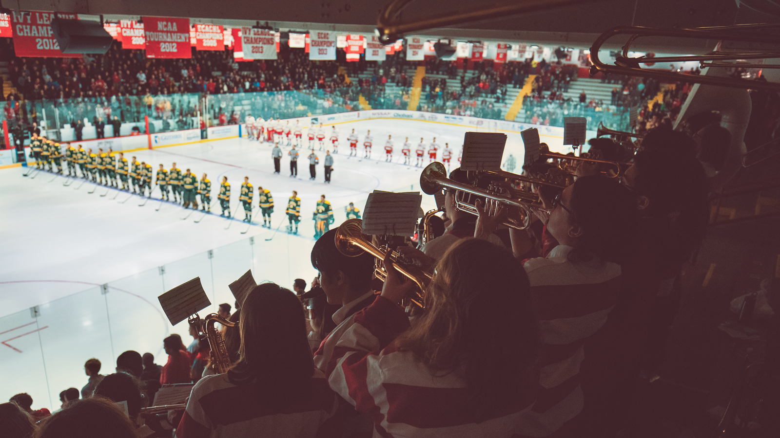 A shot of Lynah Rink at Cornell University during a men's ice hockey game, with two teams facing each other on the ice and the pep band playing in the audience.