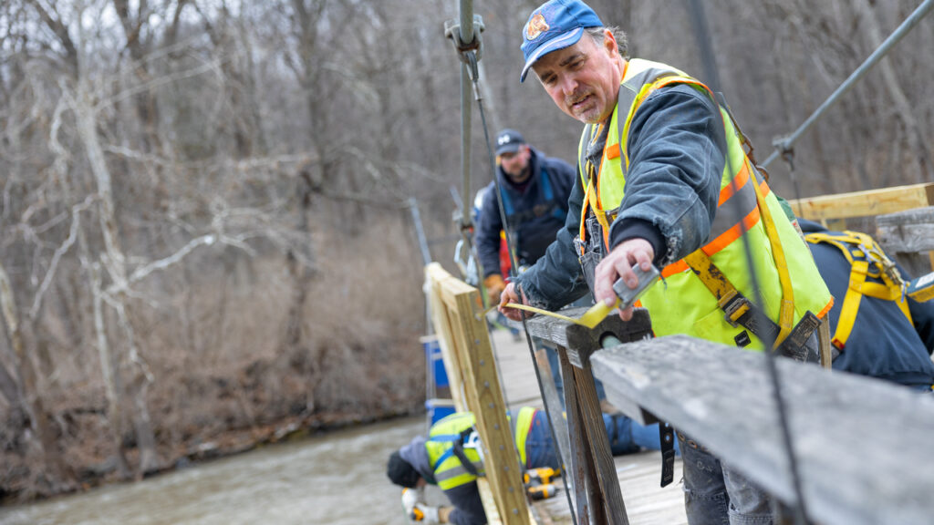 A volunteer works with his team to fit new sections of the Flat Rock pedestrian bridge.