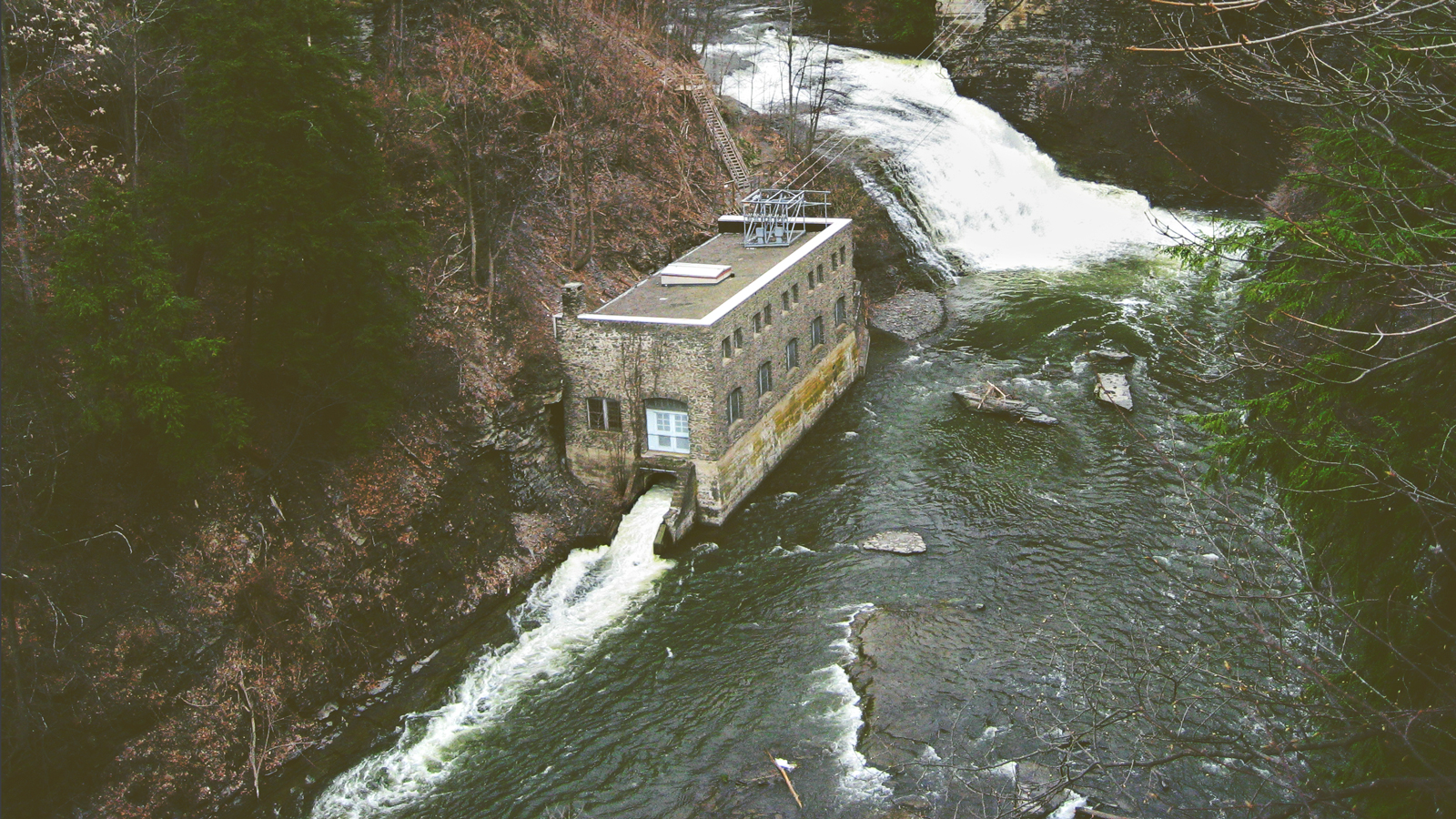A hydroelectric plant on the shore of a creek with water rushing into it from a waterfall at Cornell University