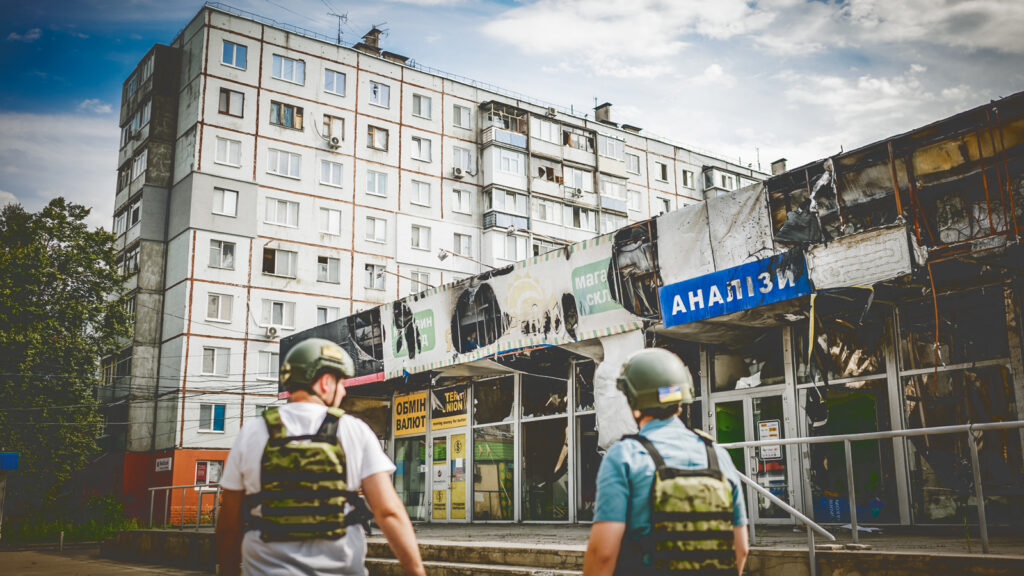 Two men walking through Kharkiv, Ukraine among buildings damaged in war.