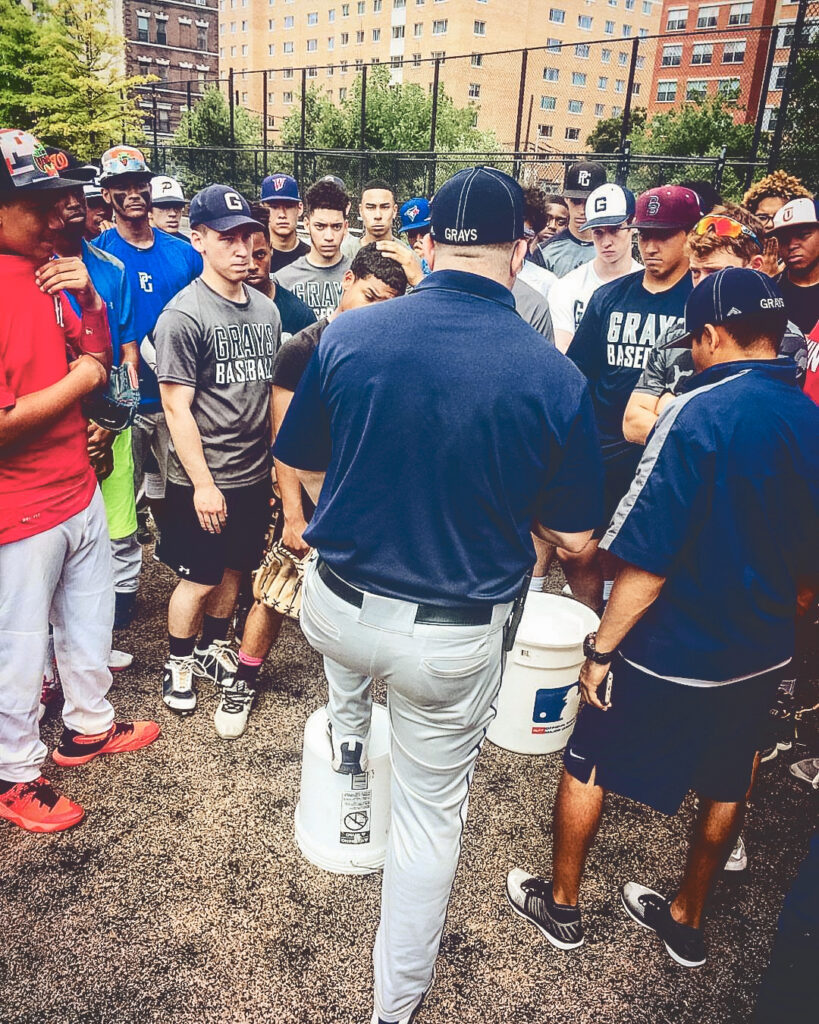 A baseball coach with his back to the camera speaks to his team of boys