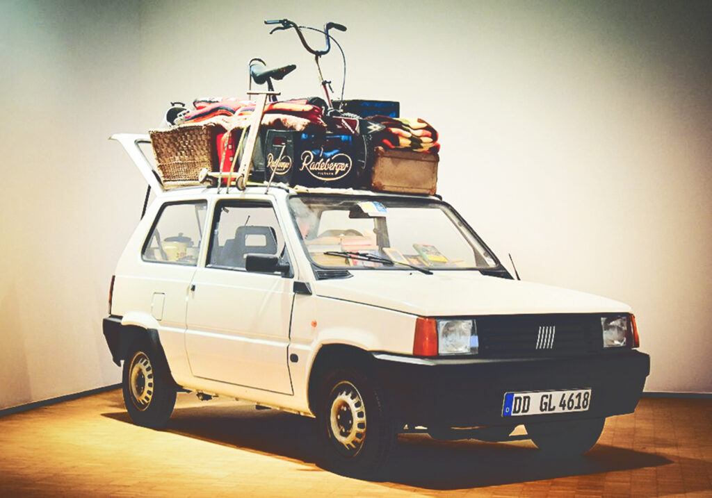 A white car with luggage and belongings on top of it on display in a museum.