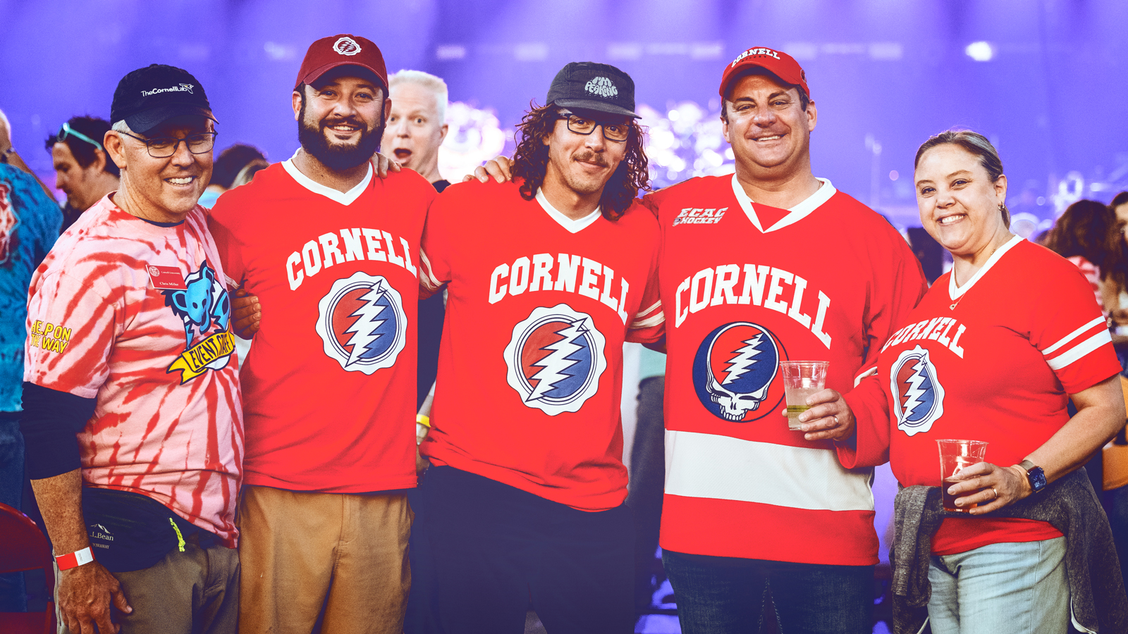 Five people stand in a row wearing Cornell Grateful Dead shirts in Barton Hall at Cornell University.