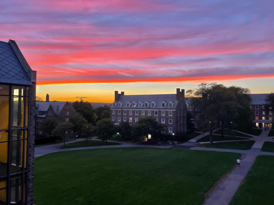 A cloud-filled sunset with blue, pink, red, and orange layers hovers in the sky over the Cornell University campus.