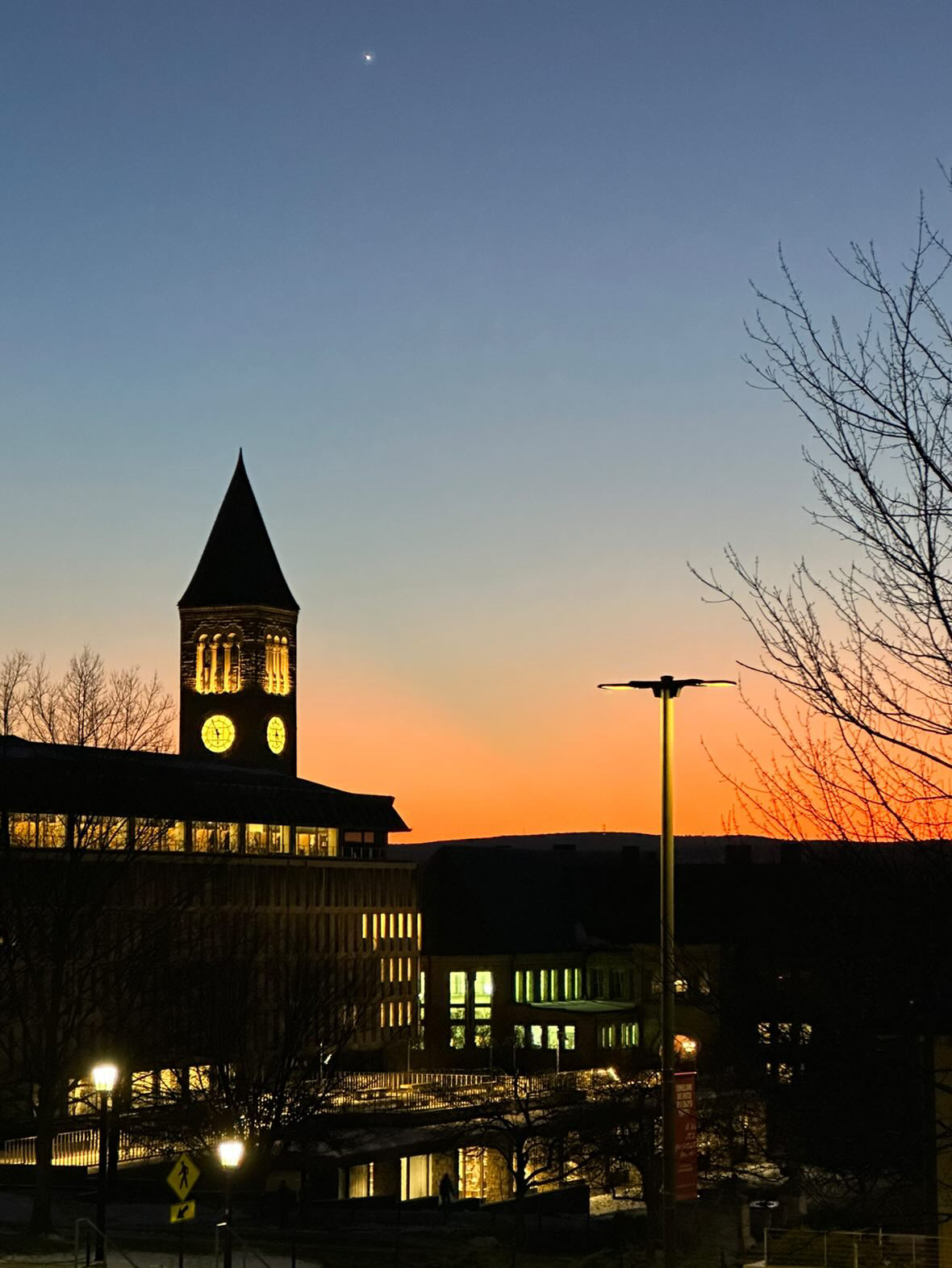 McGraw Tower at Cornell University lit up at night with an orange sunset on the horizon.