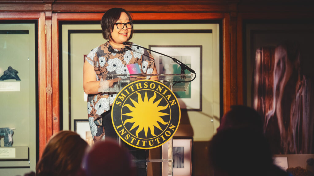 Lisa Sasaki standing at a podium with the Smithsonian Institute symbol on it