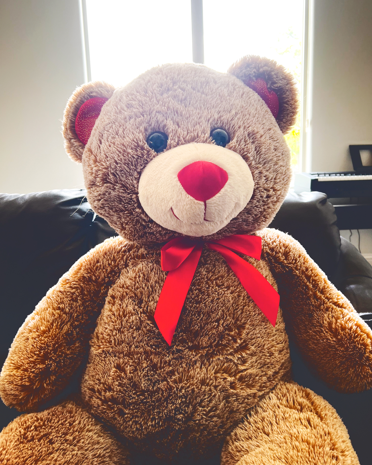 A brown teddy bear with a red bow around the neck, a red nose, and red ears