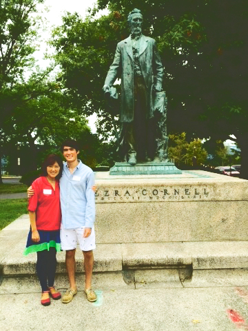 A woman and her young adult son stand next to an Ezra Cornell status