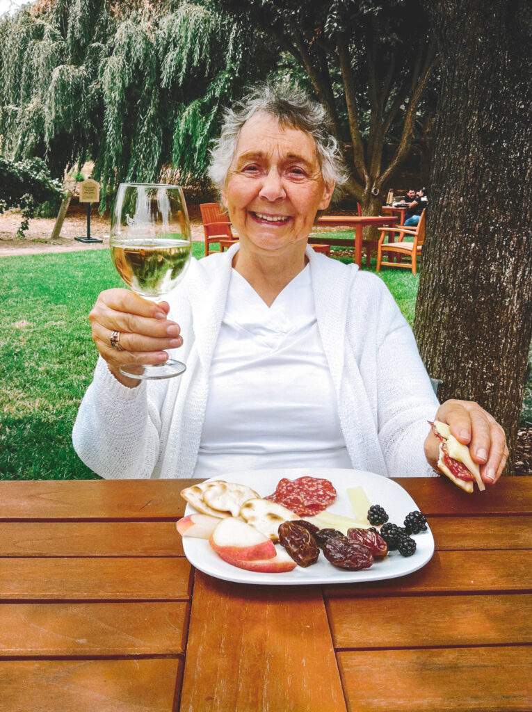 Betsy Weis eating at a table and holding a glass of wine