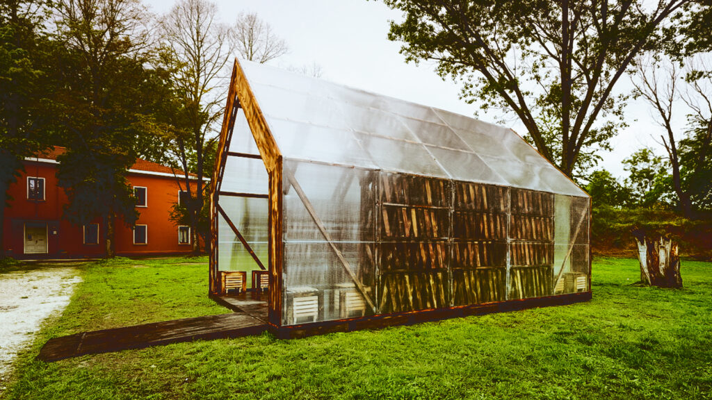 A transparent greenhouse style building with wood inside