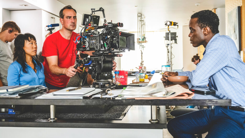 Ato Essandoh sits at a kitchen counter while being filmed for "The Diplomat"