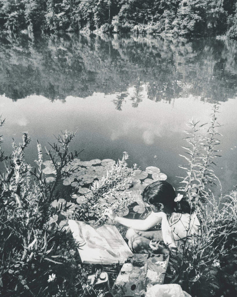 A B&W shot of a woman painting at the edge of Beebe Lake near lily pads
