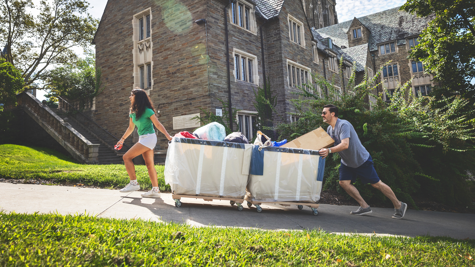 A woman pulls a large wheeling cart filled with belongings up a hill on the Cornell University