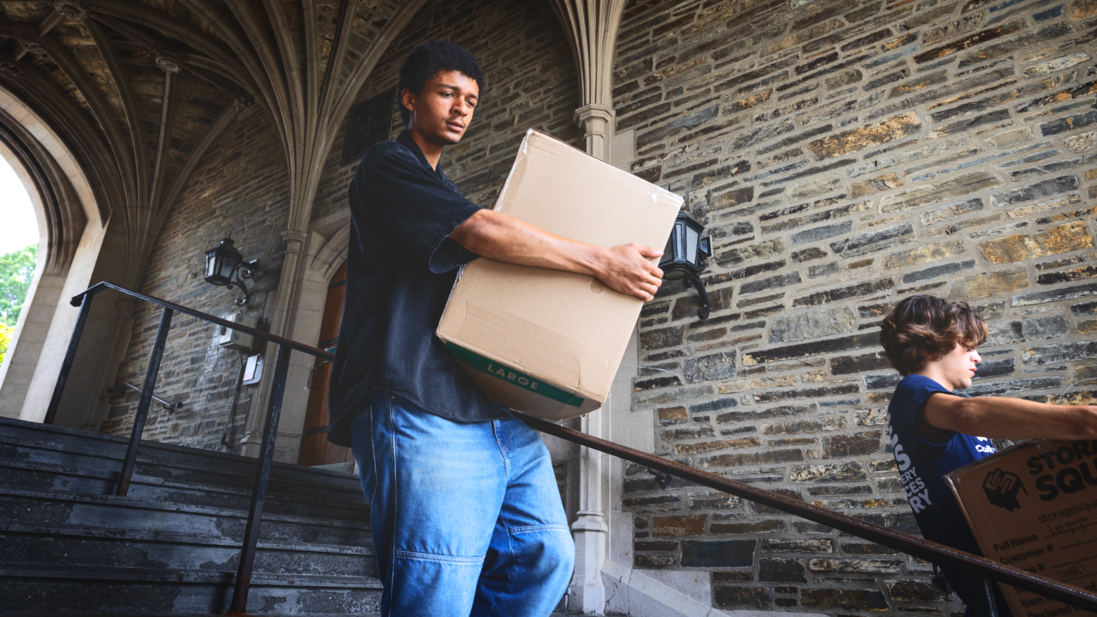 Two people carry large boxes down a flight of stairs at Cornell University.
