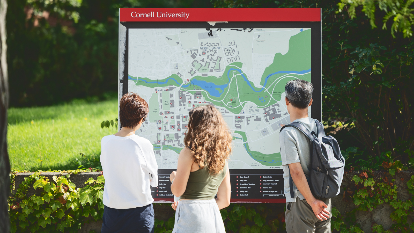 Three students with their backs to the camera look at a campus map of Cornell University.
