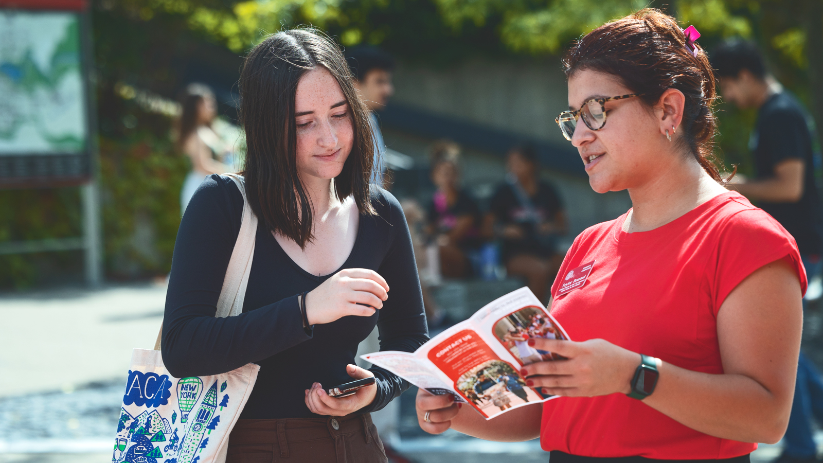 Two women look at a brochure together outside on the Cornell University campus.