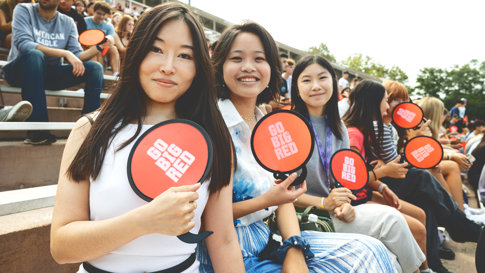Three female Cornell University students smile for the camera while holding three red disks that say Go Big Red in white letters.