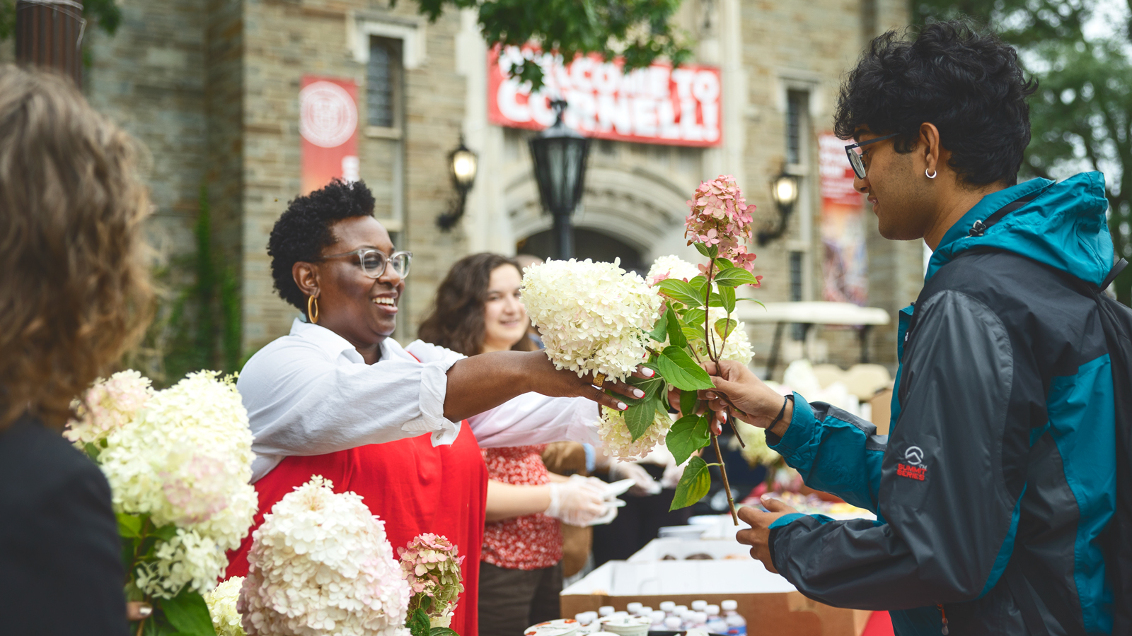 A woman hands a man a bouquet of white and pink hydrangea flowers at Cornell University.