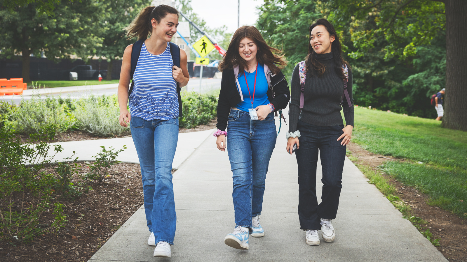 Three female students walk in a row along a sidewalk at Cornell University smiling and laughing.