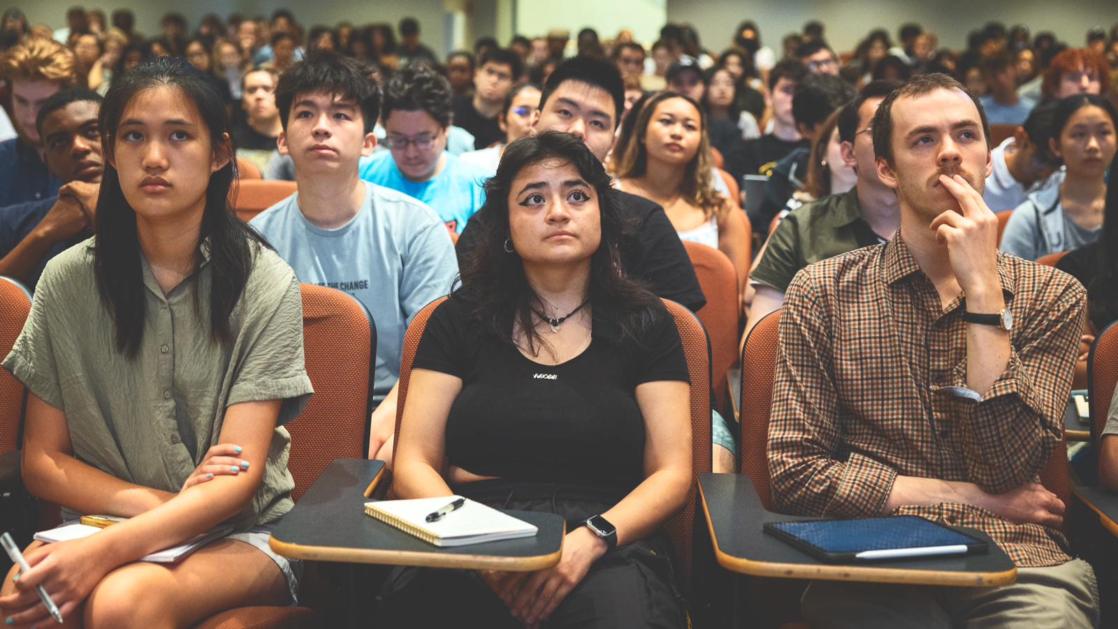 A lecture hall filled with college-aged students who are all looking in the same direction toward the front of the room.