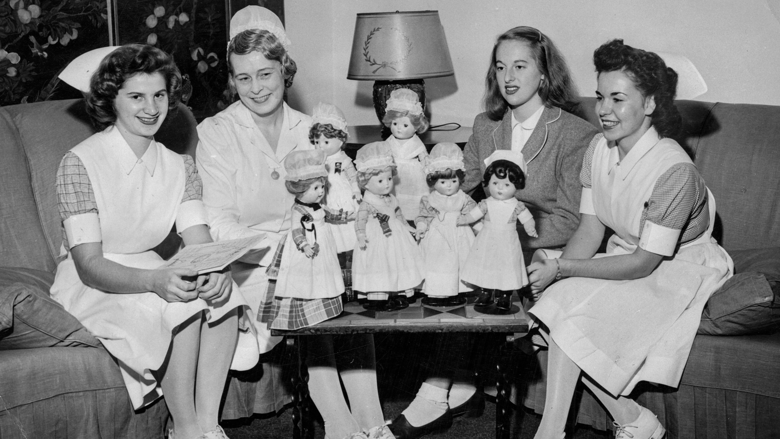 Nurses in a lounge with dolls that model student uniforms from different decades