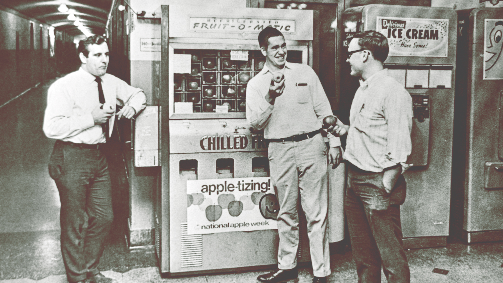 Photo shows three men enjoying apples in front of the "Fruit-o-Matic" vending machine in the Plant Sciences Building in the 1960s