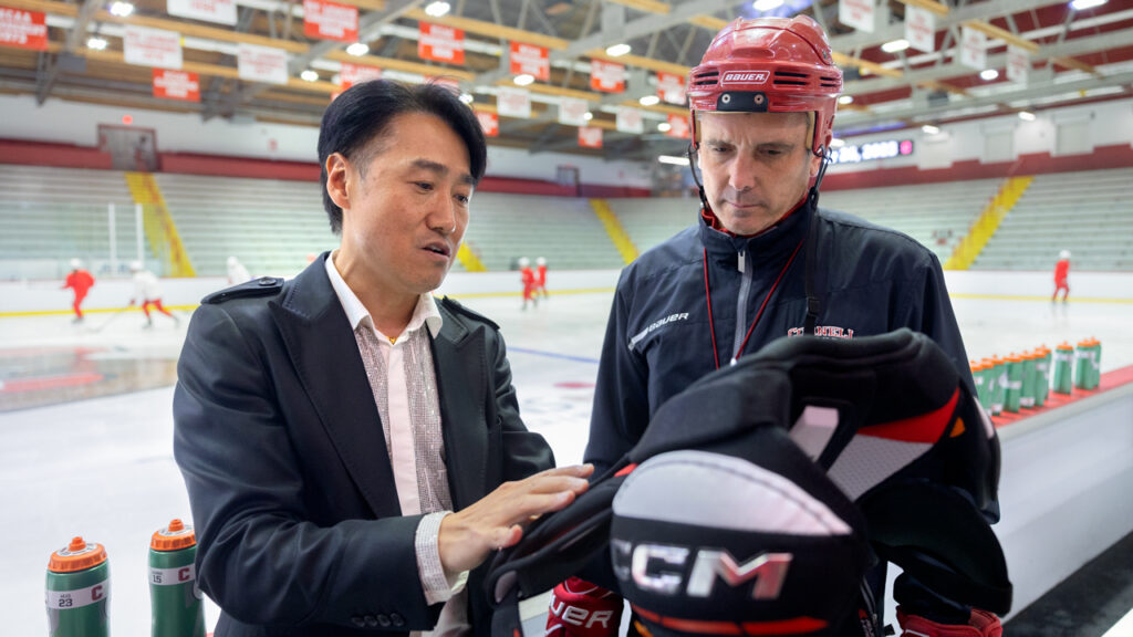 Heeju Terry Park, Associate Professor in the Department of Fiber Science & Apparel Design, speaks with Doug Derraugh, head coach of the Cornell women's ice hockey team, about hockey protective equipment ahead of practice at Lynah Rink.