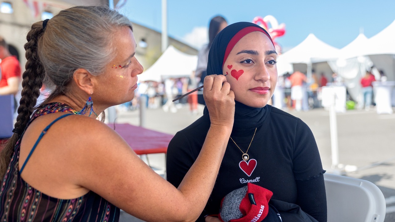 A woman paints a heart on another woman's face during the Fan Festival at Homecoming weekend