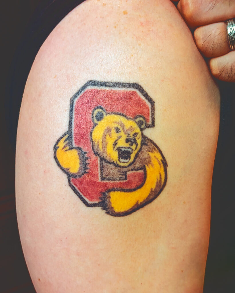 A tattoo of the Cornell University logo with a Red C and yellow bear on a man's arm