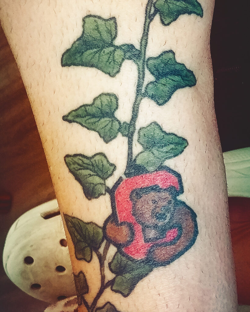 A tattoo of a red C, a brown bear and a string of green ivy