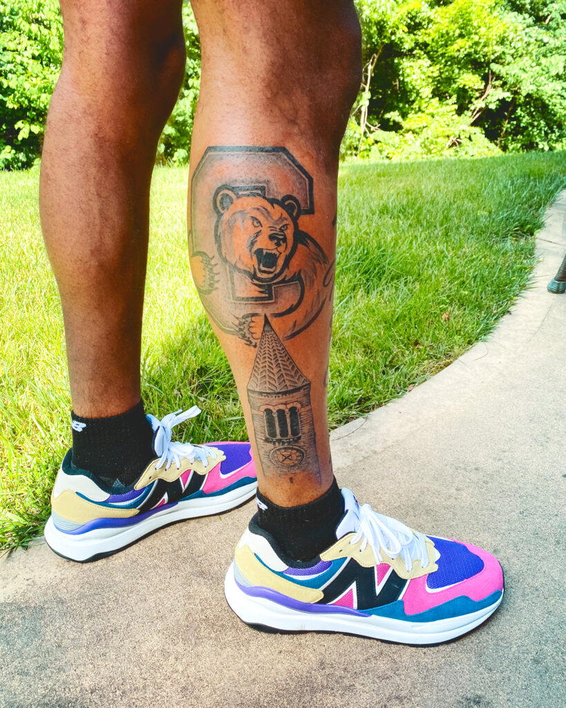 A large Cornell-inspired tattoo with a C, a bear, and a clocktower on a man's right leg