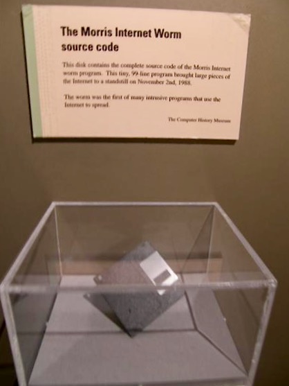 A computer disk in a clear display case in a museum with an explanatory sign reading "The Morris Internet worm source code"