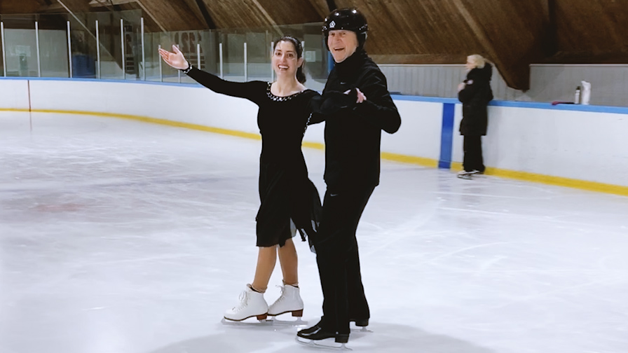 A man and a woman ice dancing on an indoor ice rink.