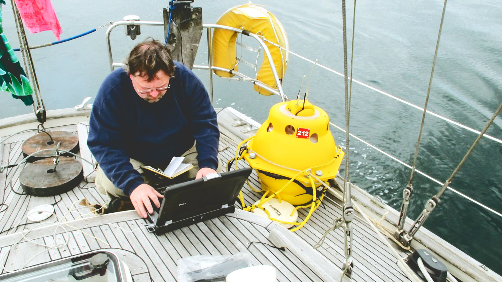 A man setting up marine audio recording equipment on a laptop on a boat.