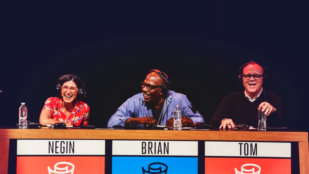 A group of three panelists participate in a live on-stage taping of a quiz show on national broadcast radio program.