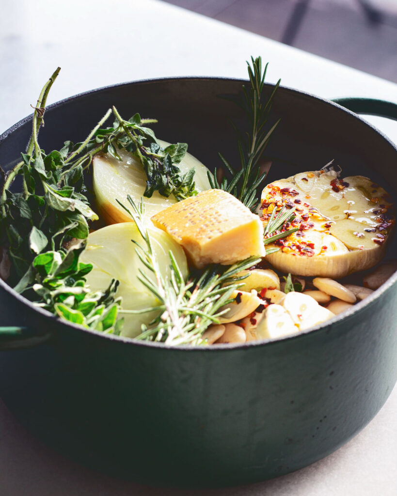 A pot of herbs, beans, vegetables, and parmesan cheese